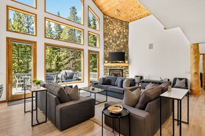 A spacious living area with a stone fireplace, multiple seating options, and large windows offering views of the outdoors. - Spacious and Peaceful 5 Mins to Ski Area/Main St (Breckenridge)