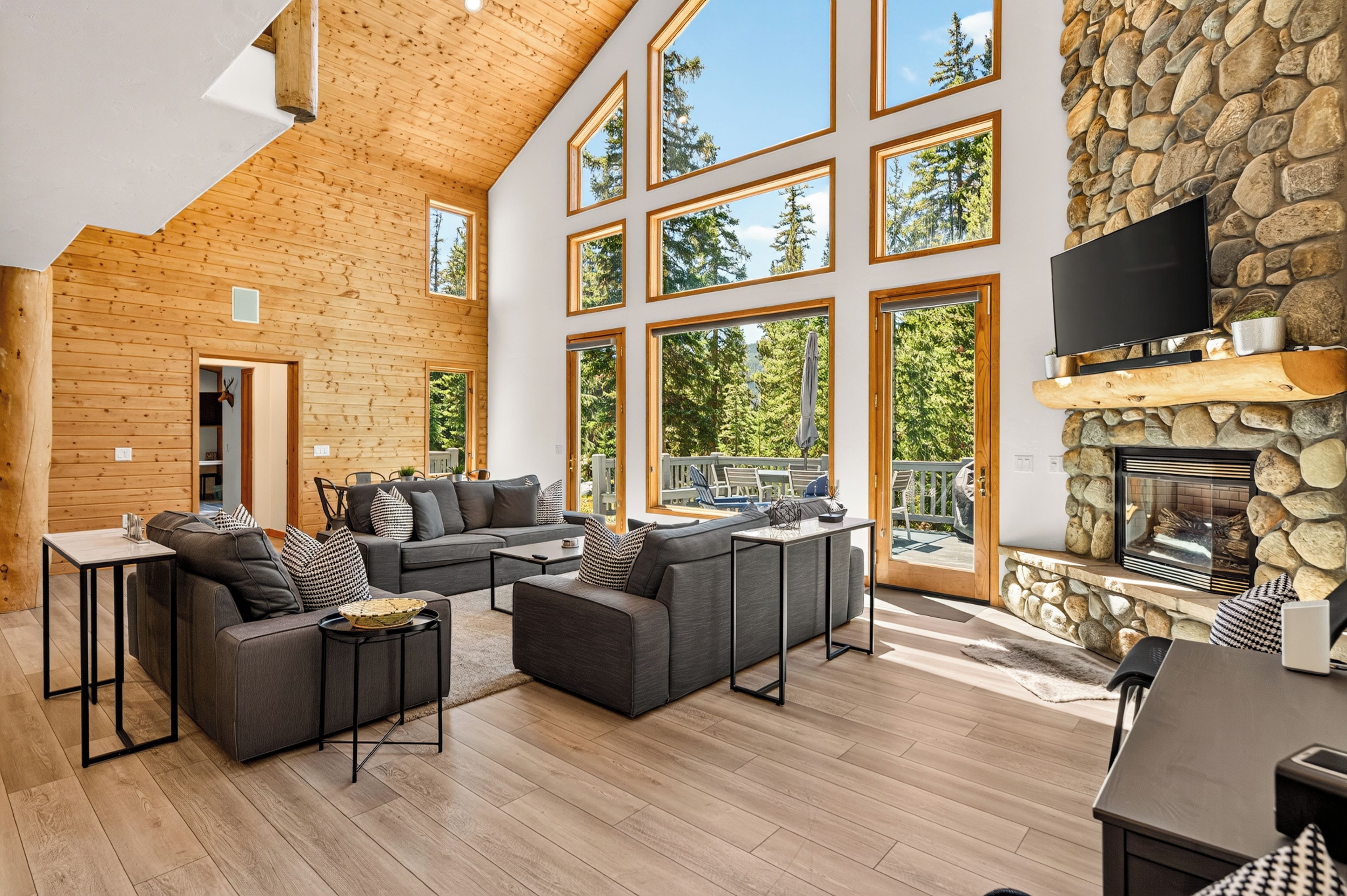 A spacious living area with a high ceiling, large windows, and a stone fireplace.