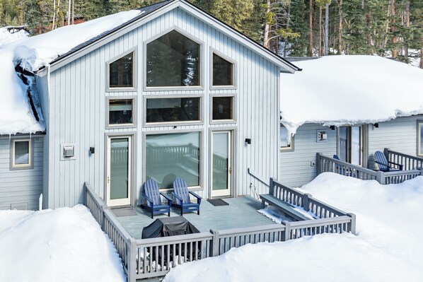 A large, light blue cabin with a covered porch and two blue Adirondack chairs.