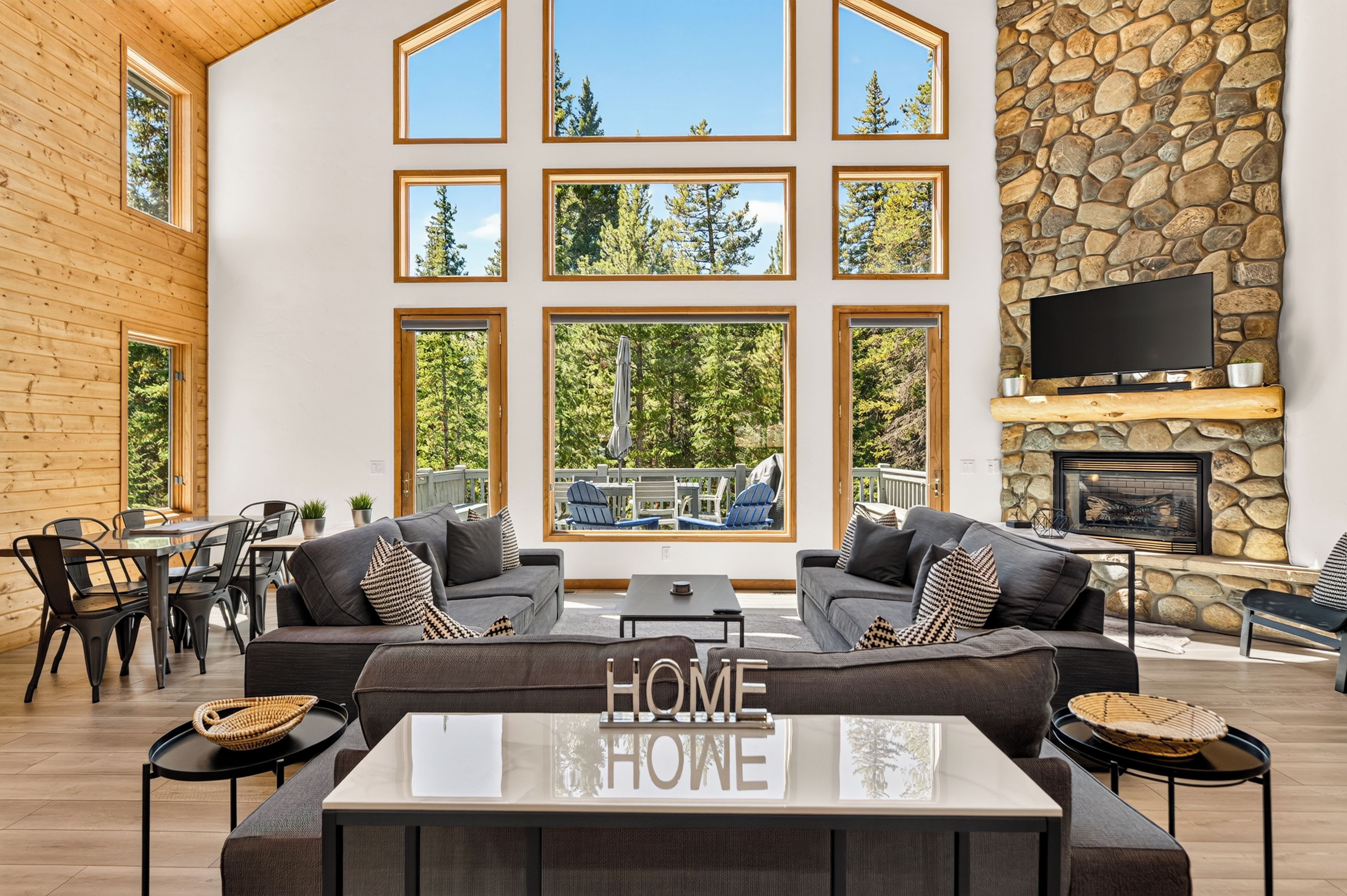 A spacious living area with a large couch, a coffee table, and a fireplace. There are multiple windows offering views of the outdoors.