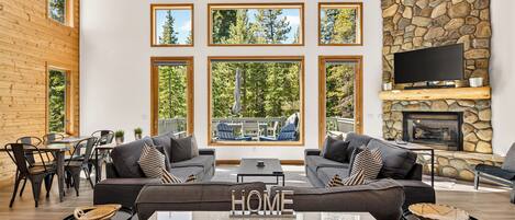 Un amplio salón con un sofá grande, una mesa de centro y una chimenea. Varias ventanas ofrecen vistas al exterior.