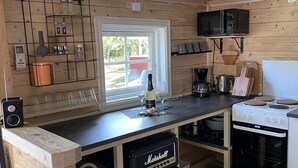Een compacte keuken met houten inrichting, een ingebouwde magnetron, een koffiezetapparaat en een compact fornuis.
