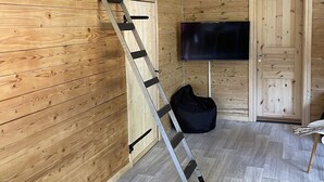 Een kamer met houten lambrisering, een aan de muur bevestigde televisie, een zwarte tas en een ladder die tegen de muur staat.