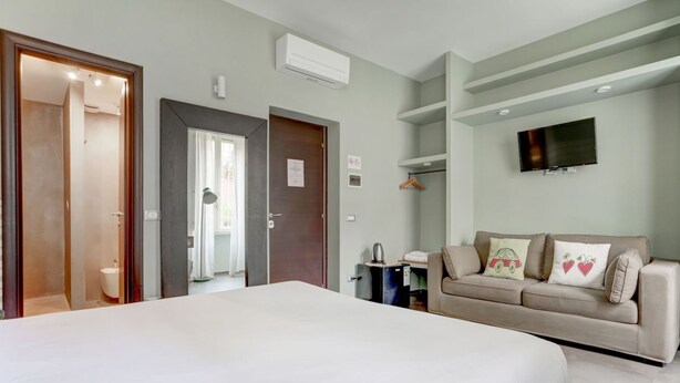 A bedroom with a large bed, a sofa, a TV, and a door leading to a bathroom. - CAPO D'AFRICA 30 COLOSSEO - HOME AND MORE (Roma)