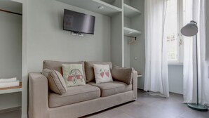 A modern living room with a beige sofa, a flat-screen TV mounted on the wall, and a floor lamp. - CAPO D'AFRICA 30 COLOSSEO - HOME AND MORE (Roma)