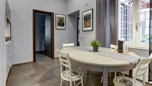 A dining area with a round table, white chairs, and a potted plant. There are framed pictures on the wall and a window with curtains. - CAPO D'AFRICA 30 COLOSSEO - HOME AND MORE (Roma)