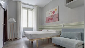 A bedroom with a bed, a sofa, a painting on the wall, and a window with curtains. - CAPO D'AFRICA 30 COLOSSEO - HOME AND MORE (Roma)