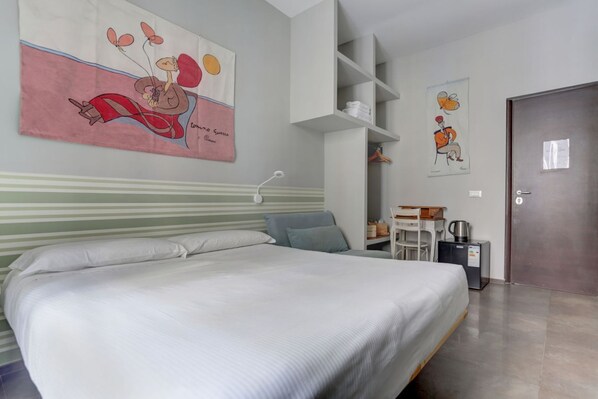 Un dormitorio con cama, cabecera, estante en la pared, una puerta y una mesita con tetera.