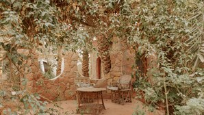 Un espacio al aire libre con paredes de piedra, muebles de madera y abundante vegetación.