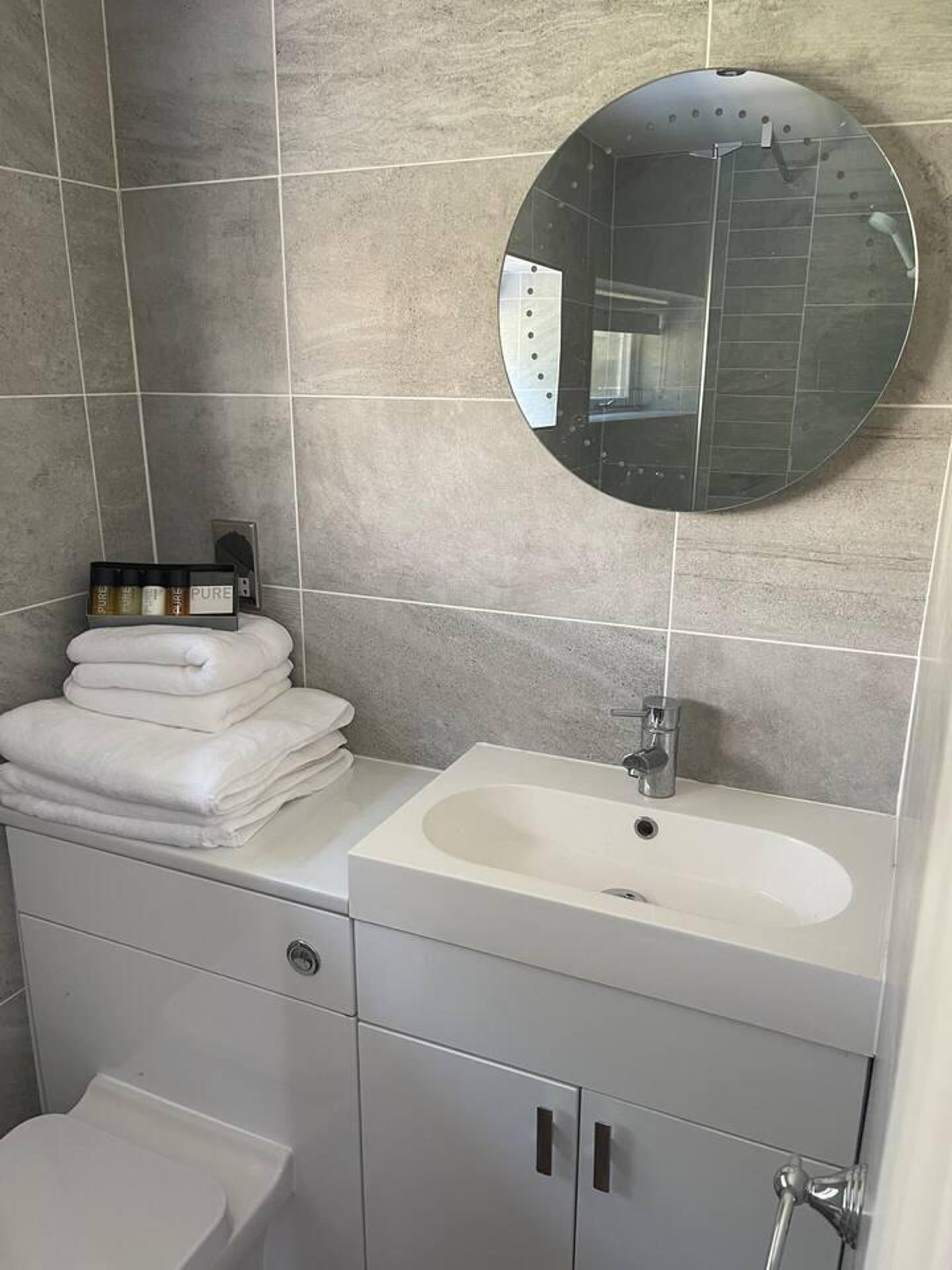 A bathroom with a round mirror, a sink, and a toilet.
