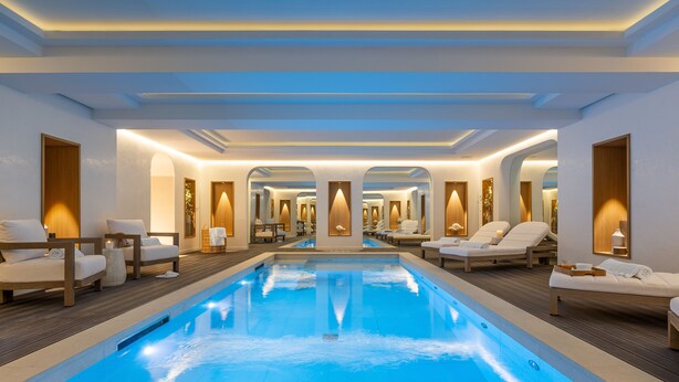 Una piscina interior moderna con sillones de descanso y suelo de madera.