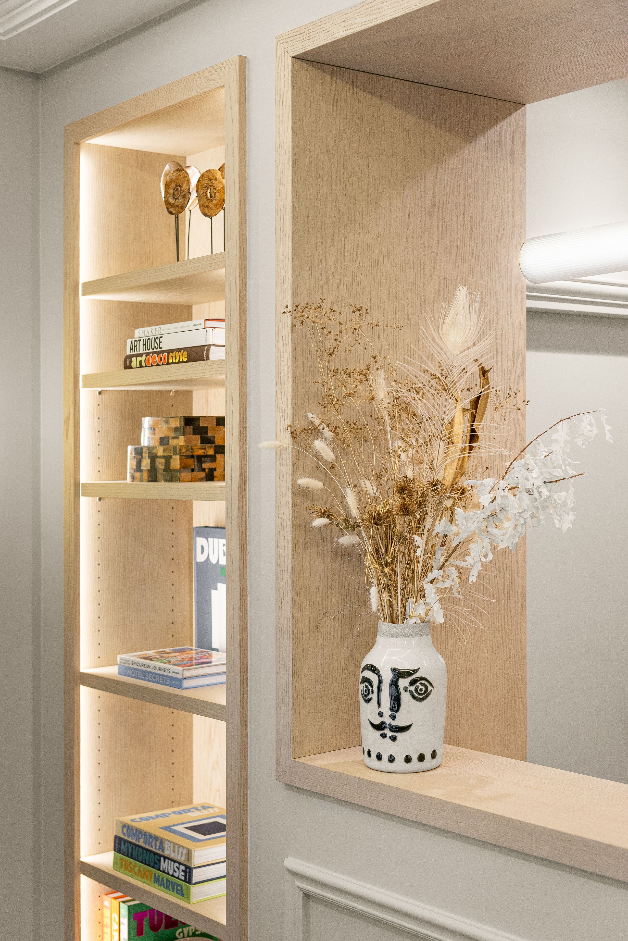 A bookshelf with books and decorative items, a vase with dried flowers, and a wooden shelf unit.