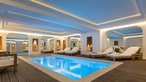 Un área interior de piscina moderna con sillones de descanso y una piscina azul cristalina.