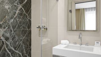 A modern bathroom with a glass-enclosed shower, a marble wall, a white sink, a mirror, and a wooden vanity.