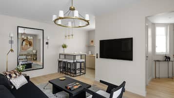 A modern living room with a black sofa, a coffee table, a chandelier, and a TV mounted on the wall.