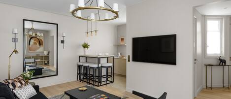 Een moderne woonkamer met een zwarte bank, een salontafel, een kroonluchter en een aan de muur bevestigde televisie.