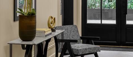 A modern interior with a black-framed door, a potted orchid, and a grey upholstered chair.