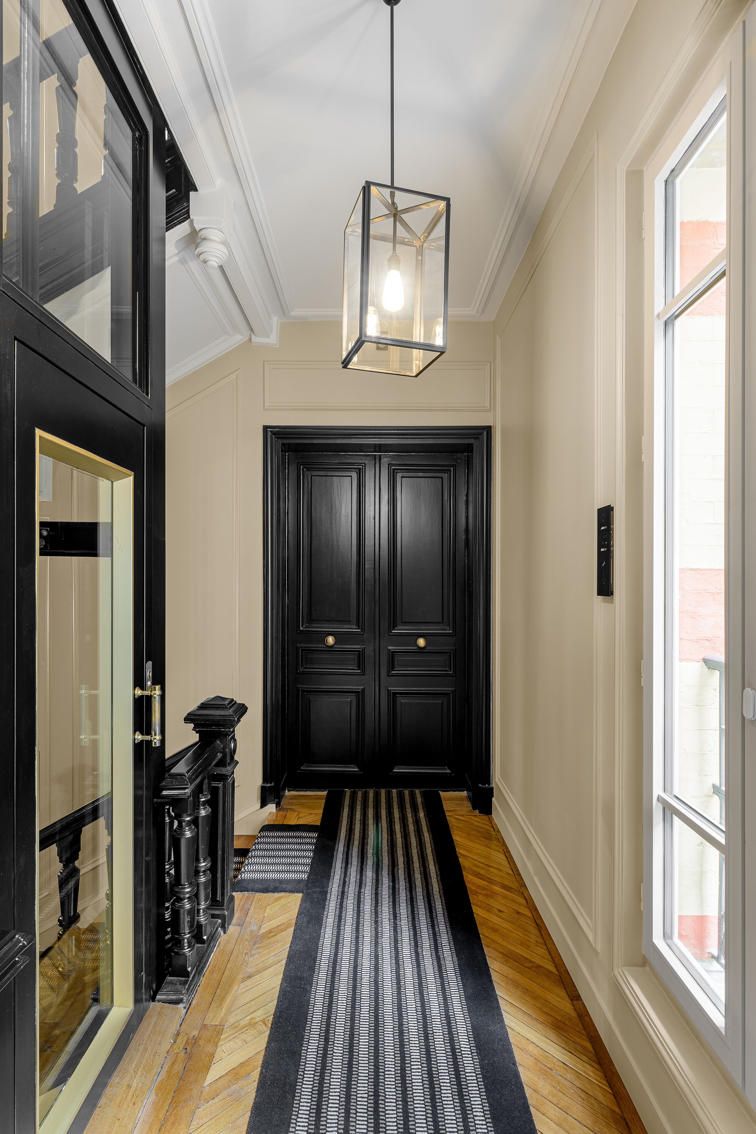 A hallway with a black door, a patterned rug, and a hanging light fixture.