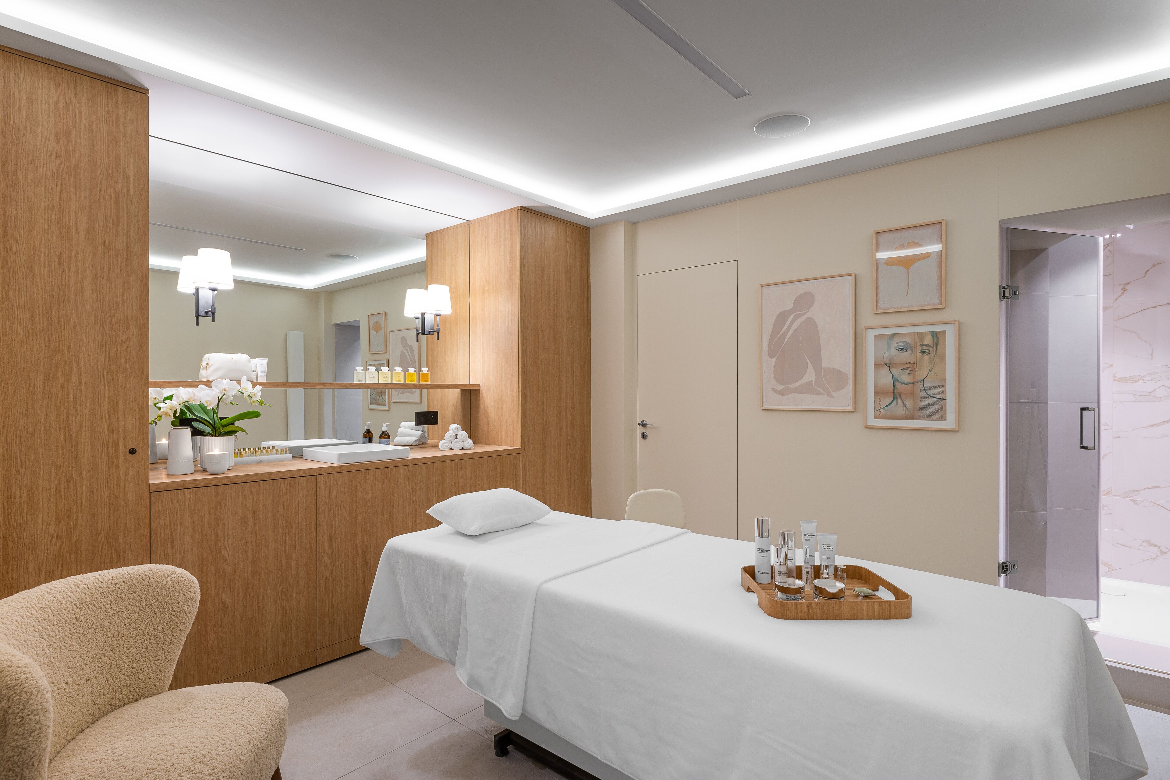 A modern hotel room with a bed, a sitting area, a vanity with toiletries, and artwork on the walls.