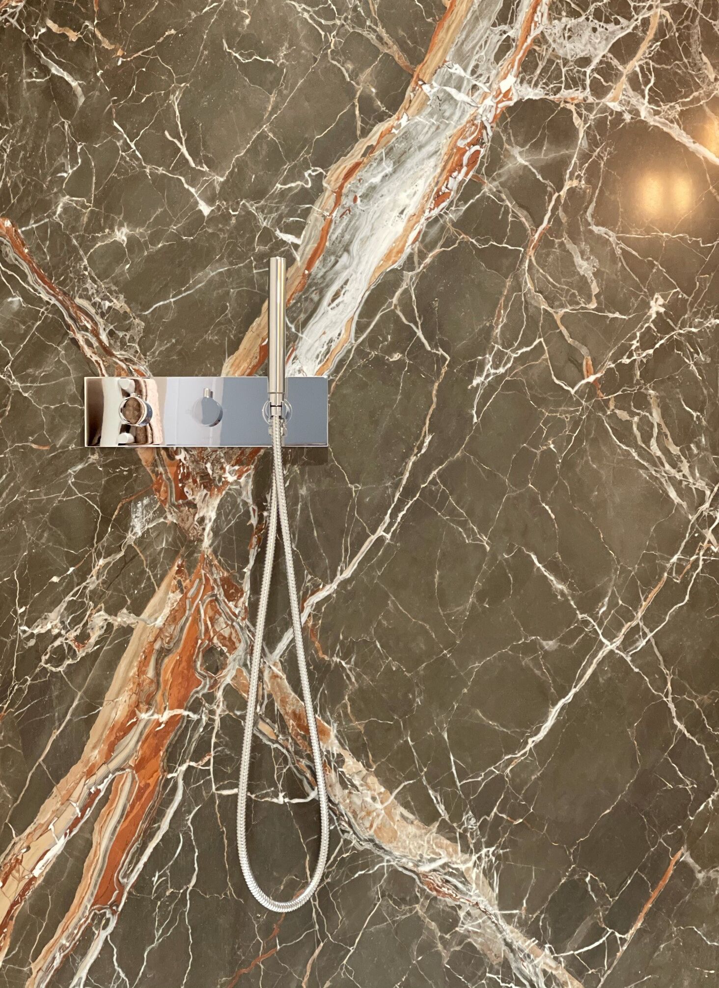 A showerhead mounted on a marble wall with a visible water hose.
