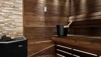 Un sauna avec des murs en bois et une section de mur en pierre, un appareil de chauffage noir et une serviette blanche sur le banc.