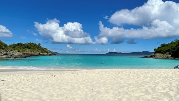 Une plage à l’eau turquoise et limpide, au sable blanc et au rivage rocheux.