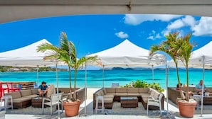 Un salon de plage avec des espaces de détente en plein air, des palmiers et une vue sur l’océan.