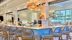 Un espace bar avec des tabourets de bar en osier, un comptoir doté d’un ordinateur et une vue sur l’espace bar.