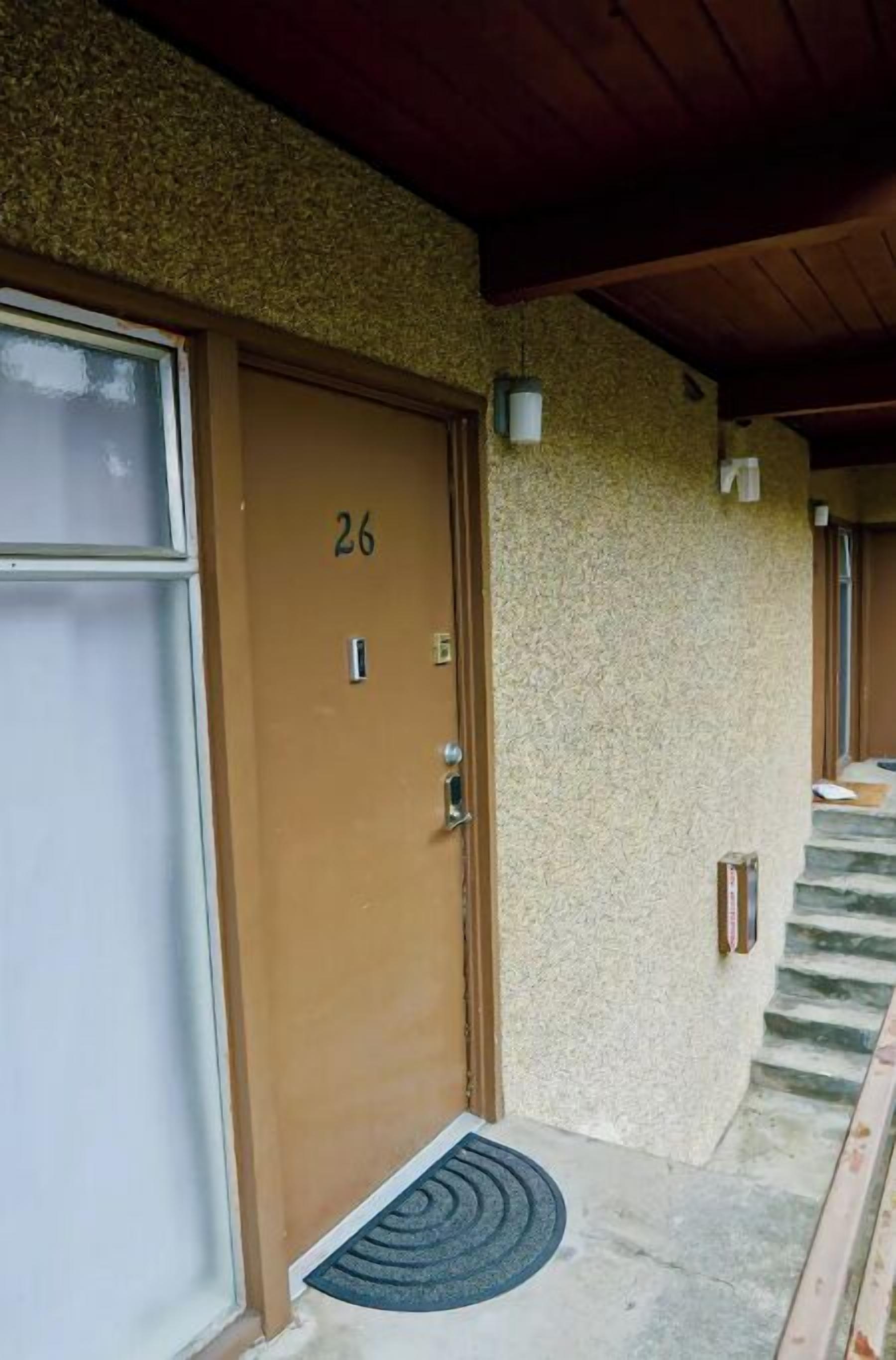 A building with a beige exterior, a brown door labeled '26', and a small staircase leading to an upper level.