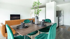 A modern dining area with a wooden table, green velvet chairs, and a vase with green plants.