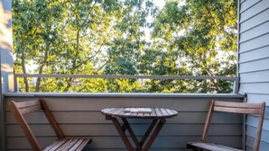 A balcony with two wooden chairs and a small round table, overlooking a tree-filled area. - Stylish 2 Bedroom Capitol Hill Apartment (Seattle)