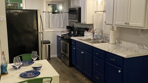 A compact kitchen with white and blue cabinets, a dining table with chairs, and a wood floor. - Cute, cozy, updated cottage just steps from gorgeous Houghton Lake (Prudenville)