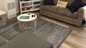 A living room with a sofa, a coffee table, a TV, and a bookshelf. - Cute, cozy, updated cottage just steps from gorgeous Houghton Lake (Prudenville)