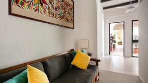 A living room with a sofa, pillows, a framed abstract painting, a lamp, and a view of a patio with plants. - Casitas Miramar Puerto Vallarta Malecón (Puerto Vallarta)