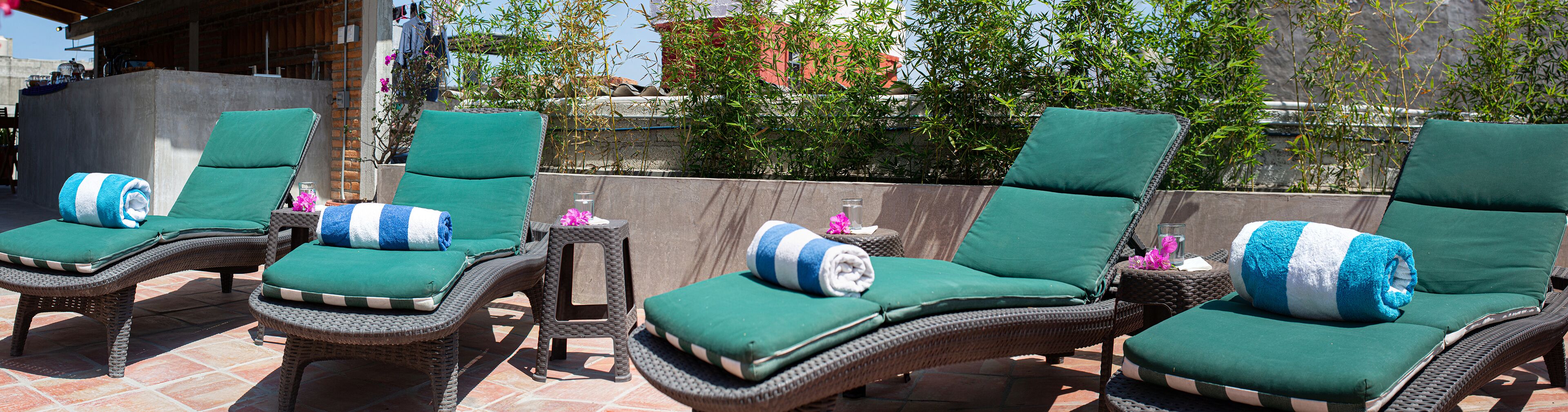 A patio area with wicker lounge chairs and green cushions, a small table with a glass, and a backdrop of bamboo plants.