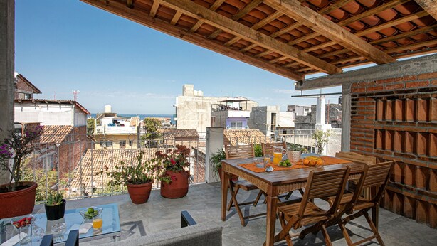 A rooftop terrace with a wooden table and chairs, potted plants, and a clear view of the cityscape. - Casitas Miramar Puerto Vallarta Malecón (Puerto Vallarta)
