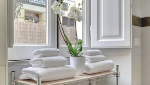 A bathroom with a window, a shelf with folded towels, a potted plant, and a decorative shell.