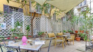An outdoor patio area with a table and chairs, surrounded by potted plants and a lattice fence.