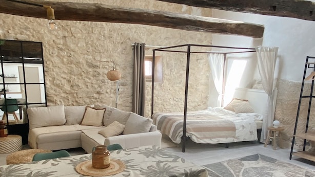 Un salón acogedor con un sofá modular, una mesa de comedor con sillas, una cama con dosel y una pared de piedra.