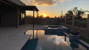 Piscina con una pérgola y un muro de ladrillo, al atardecer.