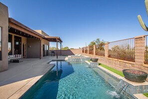 A swimming pool with a patio area, a pergola, and a brick wall with a fence.