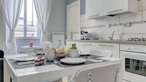 A modern kitchen with white cabinets, a gas stove, and a window with white curtains. - APPARTAMENTO SANTI QUATTRO 2 - HOME AND MORE (Roma)