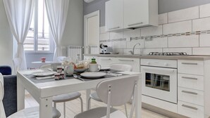 A modern kitchen with white cabinets, a built-in oven, and a dining area with a table set for two. - APPARTAMENTO SANTI QUATTRO 2 - HOME AND MORE (Roma)