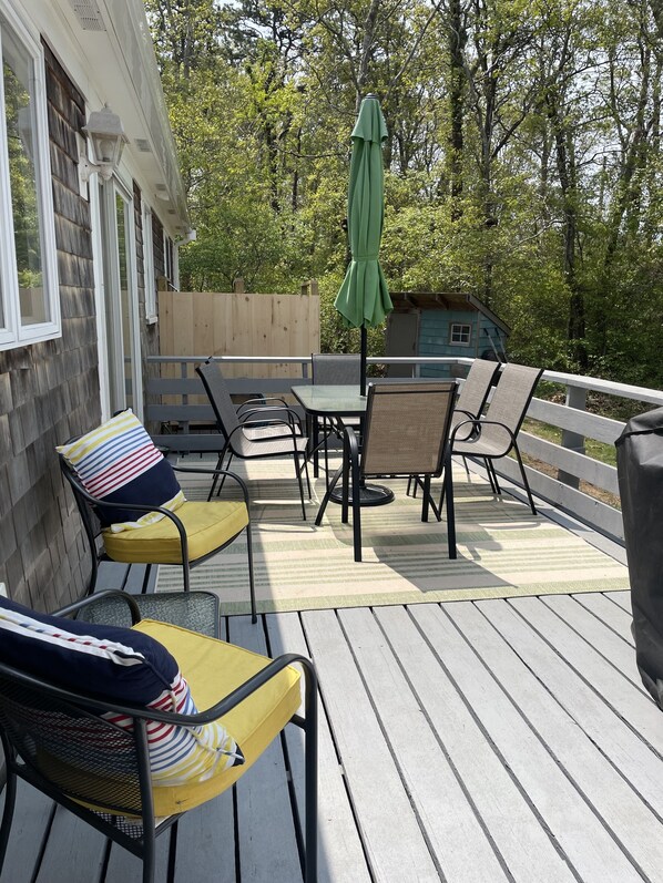 An outdoor deck with a table and chairs, a green umbrella, and a wooden fence.