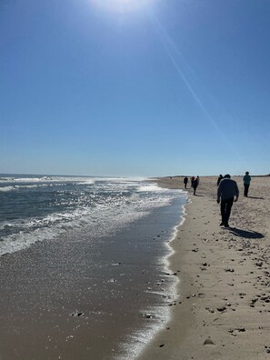 A beach with people walking along the shore, waves crashing onto the sand, and a clear blue sky.