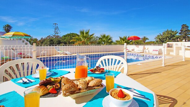 A dining table with breakfast items, a pool, and umbrellas. - Heatable pool & BBQ retreat in Carvoeiro (Carvoeiro)
