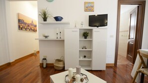 En stue med et fladskærms-tv, et maleri, en skål, stearinlys og en bakke med stearinlys og en plante.
