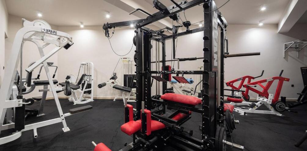 Ein Fitnessstudio mit verschiedenen Trainingsgeräten, darunter ein Squat-Gestell und Gewichtbänke.