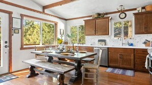 A rustic kitchen with wooden cabinets, a large window, and a dining area with a bench. - Monterey Log Lair With Pool Table - Slope Views (Big Bear Lake)