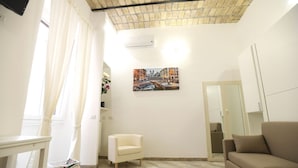 Un salon avec un plafond en briques, un canapé, un fauteuil, une table et un tableau accroché au mur.